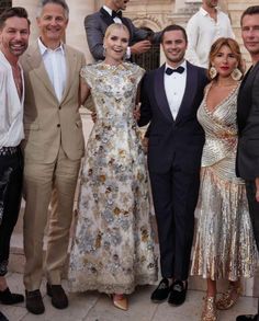 a group of people standing next to each other in front of a building wearing tuxedos