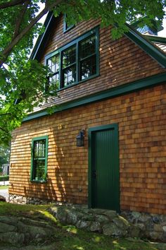 a brown house with green doors and windows on the outside, surrounded by grass and trees