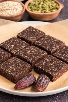 some brownies are on a plate with nuts and seeds next to it, along with other ingredients