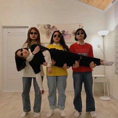 three girls standing in a room with one holding a large object and the other wearing sunglasses