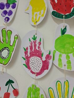 handprints are hanging from clothes pins on a white wall with fruit and vegetables painted on them