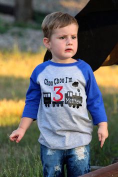 a little boy standing in the grass with an umbrella behind him and wearing a shirt that says choo choo i'm 3