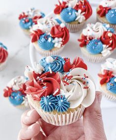 a person holding a cupcake with red, white and blue frosting on it