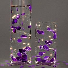 two tall vases with purple flowers and lights in them, one is filled with water