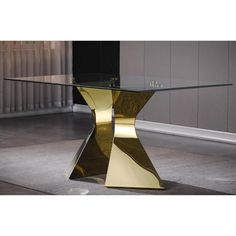 a glass table with gold colored legs and a metal base on the floor in front of a gray wall