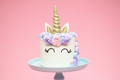 a white cake with pink and blue flowers on it's face is decorated like a unicorn