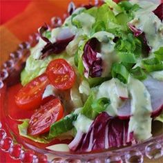 a salad with dressing and tomatoes in a glass bowl on a red tableclothed cloth