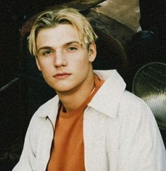 a young man with blonde hair sitting in front of a car