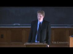 a man standing at a podium in front of a blackboard