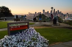 people are walking around in the park with flowers on the ground and buildings in the background