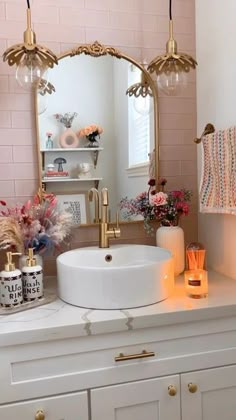 a bathroom sink with lights above it and flowers in vases on the counter top