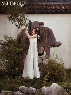 a woman in a white dress standing next to a rock and holding a black umbrella