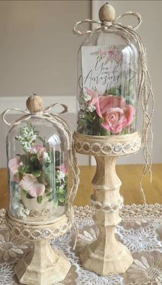 two glass jars with flowers inside sitting on a lace covered tableclothed table cloth