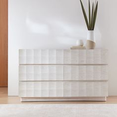 a large white dresser sitting on top of a hard wood floor next to a plant