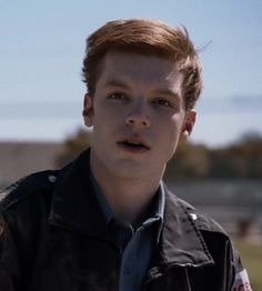 a young man wearing a jacket and tie standing in front of a fenced area