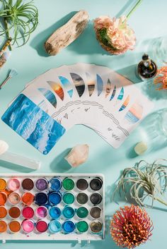 an assortment of art supplies and flowers on a blue background with watercolor paints, brushes, and other items