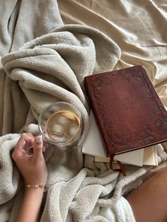 a person laying in bed with a book and cup of coffee next to it on top of a blanket