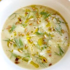 a white bowl filled with soup and garnished with green onions, pine nuts and dill