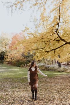 a woman is walking through the leaves in an autumn park