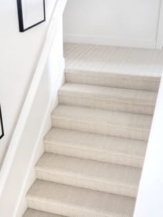 the stairs in this house are lined with white carpet and black framed pictures on the wall