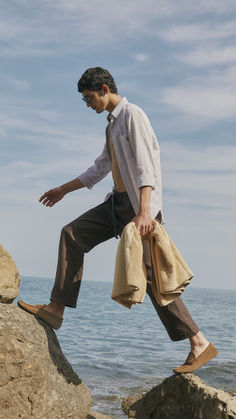 a man standing on top of a rock next to the ocean with his hand in his pocket