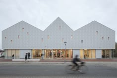 people are walking and riding bikes in front of a building with three triangular shaped windows