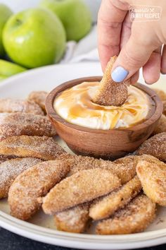 a person dipping something in a bowl with sugar on top of some breaded pastries