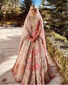 a woman in a bridal gown standing on a stone walkway with trees and bushes behind her