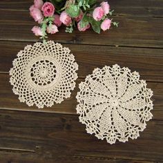 two crocheted doily are sitting on a wooden table next to pink roses