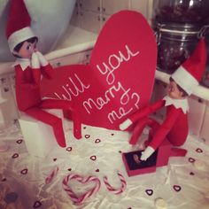 two elfs sitting on top of a table next to a heart shaped sign that says will you marry me?