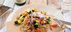 a white plate topped with pasta and veggies next to a bottle of wine