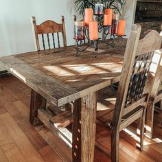 a wooden table with chairs and candles on top of it in front of a window