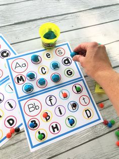 two hands are playing with letters and shapes on the table, while another hand is holding a plastic cup