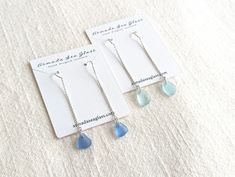 two pairs of earrings with blue tears are on a white cloth background and one is in the foreground