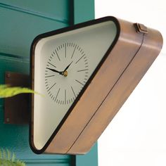 a clock mounted to the side of a green door next to a potted plant