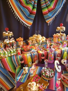 a table filled with lots of food and desserts on top of colorful cloth covered tables