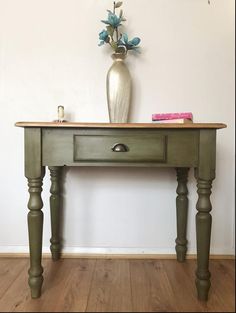 a vase with flowers on top of a wooden table in front of a white wall