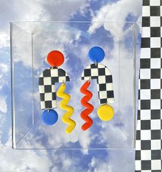 a pair of colorful earrings sitting on top of a glass case next to a checkered wall