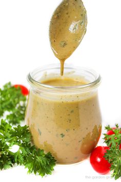 a spoon full of dressing with parsley on the side and tomatoes in the background