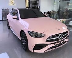 a pink car is parked in front of a glass display case at a mercedes dealership