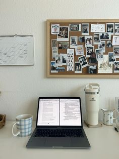 an open laptop computer sitting on top of a desk next to a cup and coffee mug