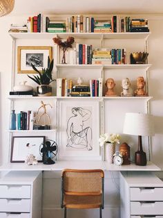 a white desk topped with lots of drawers under a window next to a lamp and bookshelf