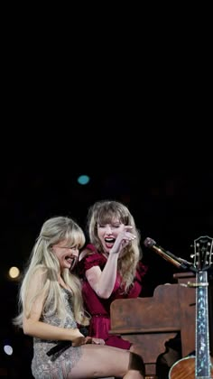 two women sitting on top of a piano next to each other in front of a microphone