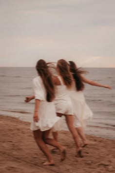 three girls running on the beach with their arms around each other and one girl in white dress