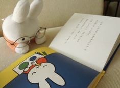 an open book sitting on top of a couch next to a stuffed animal and glasses