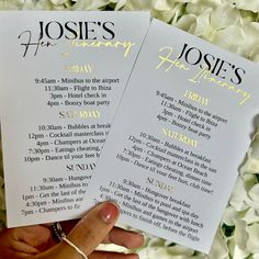 two wedding program cards held up in front of white flowers with gold lettering on them