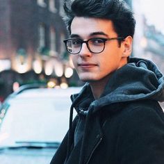 a young man wearing glasses standing on the street