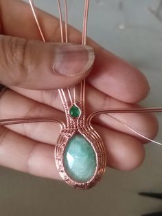 a person holding a piece of wire with a green stone in it's center