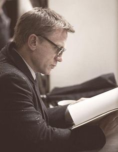 a man sitting at a table with a book in his lap and looking down on the paper