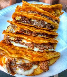 a white plate topped with lots of tacos covered in cheese and sauces on top of each other